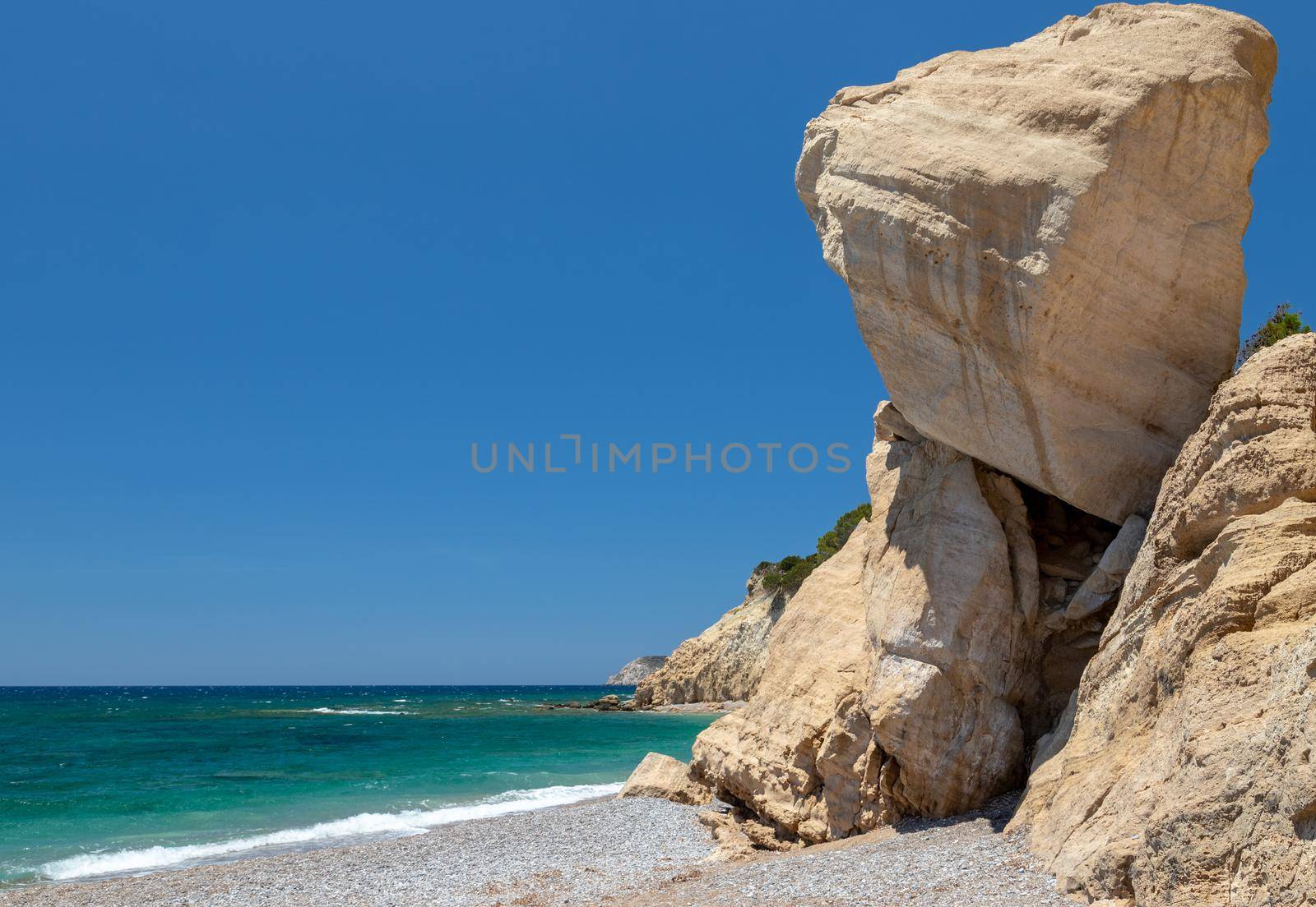 Gravel / pebble beach Akra Fourni nearby Monolithos  at Rhodes island with multi colored ocean water, waves and rock formation