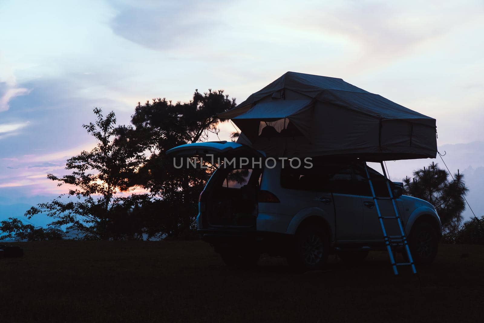 A car with a tent on the roof, parked at top mountain in the evening.