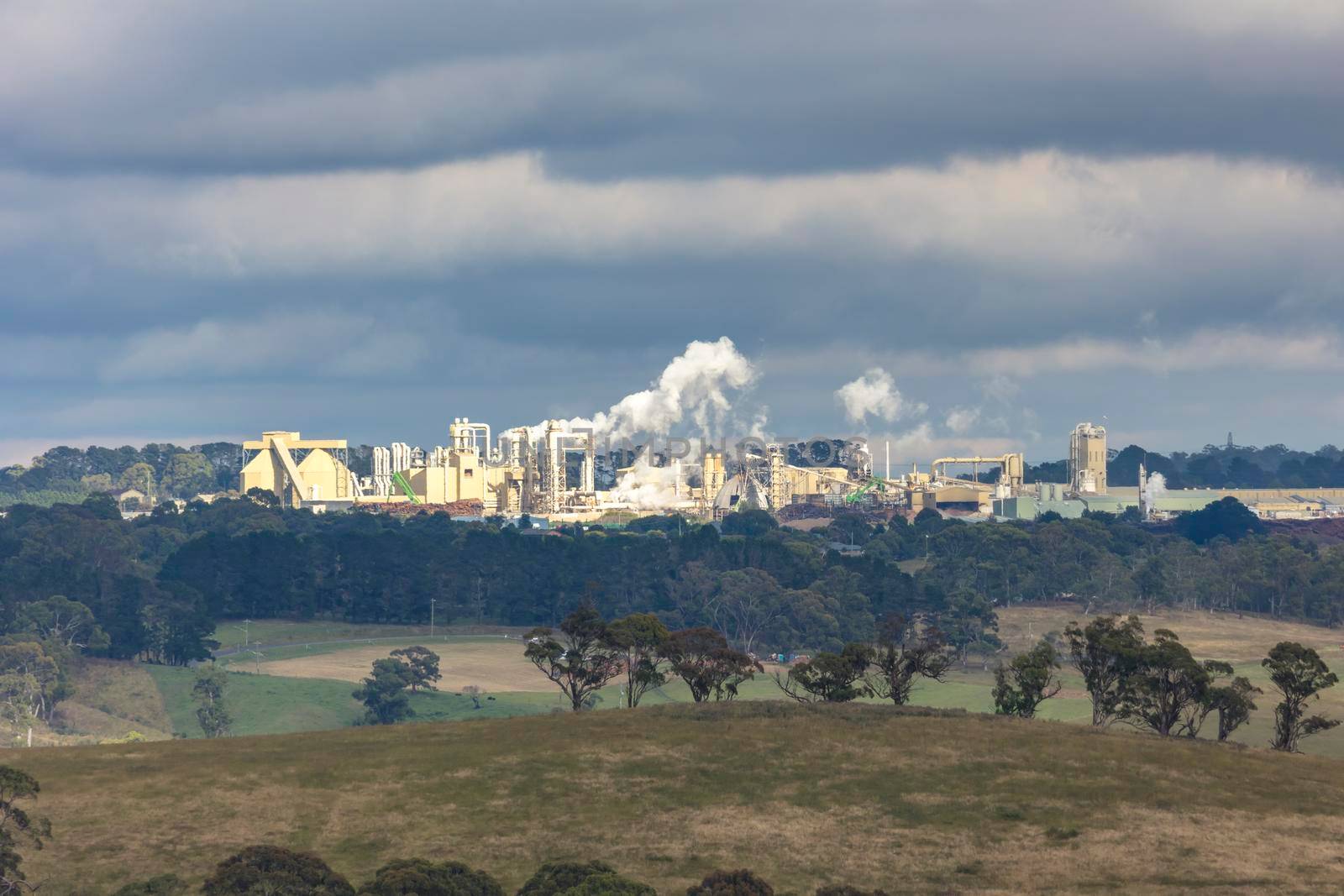 A large manufacturing facility in a regional township with steam coming from the chimney stacks during processing