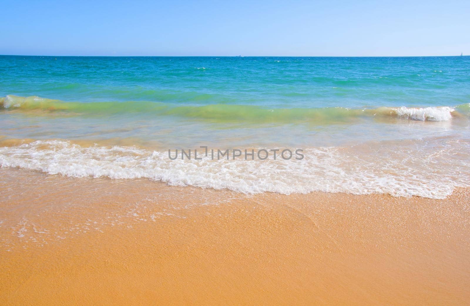 Ocean shore with yellow sand, blue water and waves, summer, Portugal