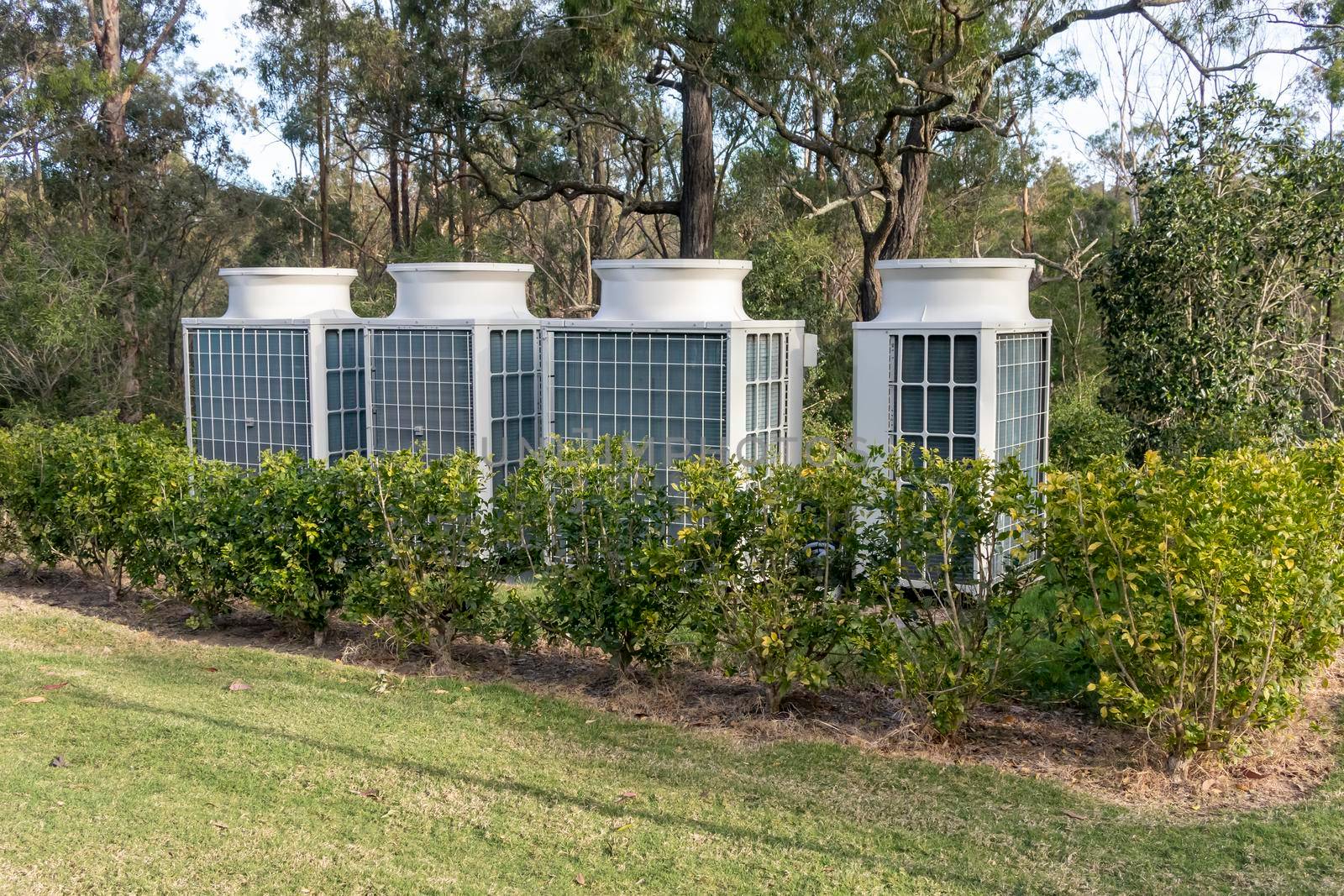 Air conditioner cooling towers outside in a garden surrounded by plants and trees