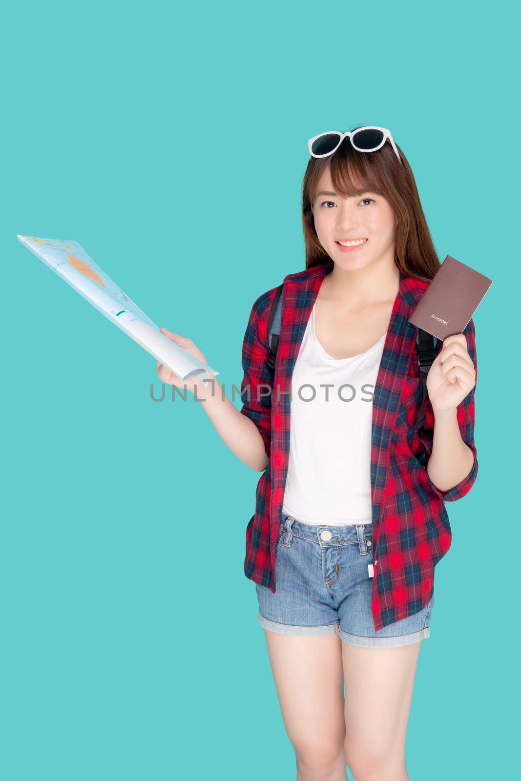 Beautiful portrait young asian woman wear sunglasses on head smile excited and enjoy summer holiday isolated blue background, girl hipster cheerful holding passport and map for travel trip concept.