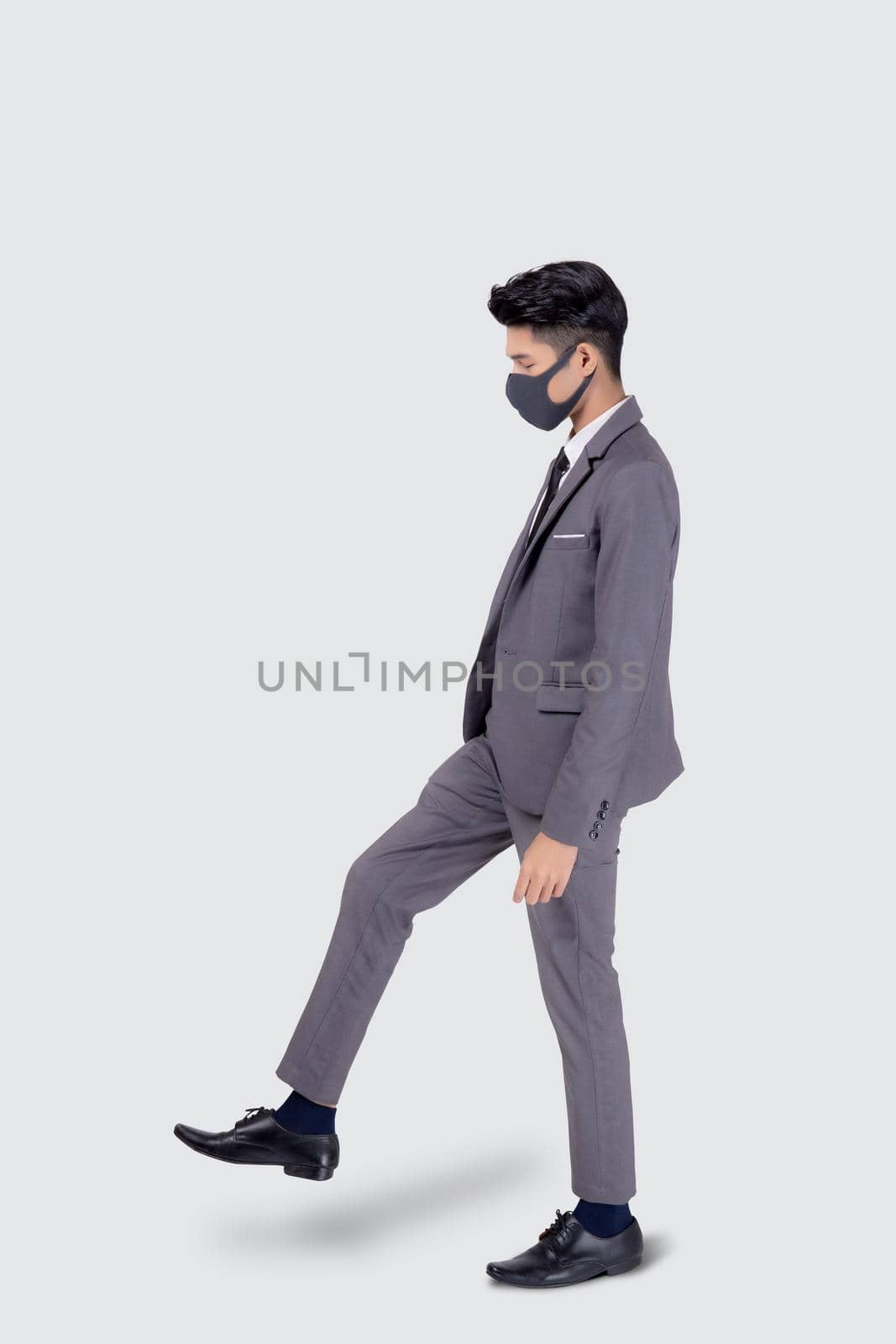 Portrait young asian businessman in suit wearing face mask walk step for protective covid-19 isolated on white background, business man and healthcare, quarantine for pandemic coronavirus, new normal.