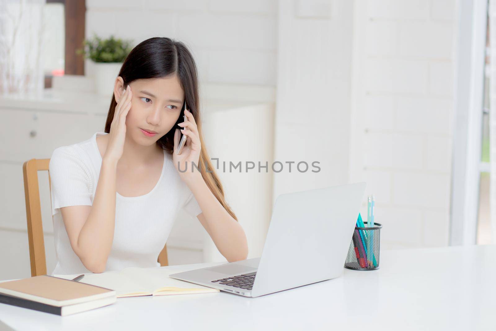 Young asian woman working on laptop computer and talking smartphone having stress and upset at home, girl having problem and worried, frustrated and unhappy, business and communication concept. by nnudoo