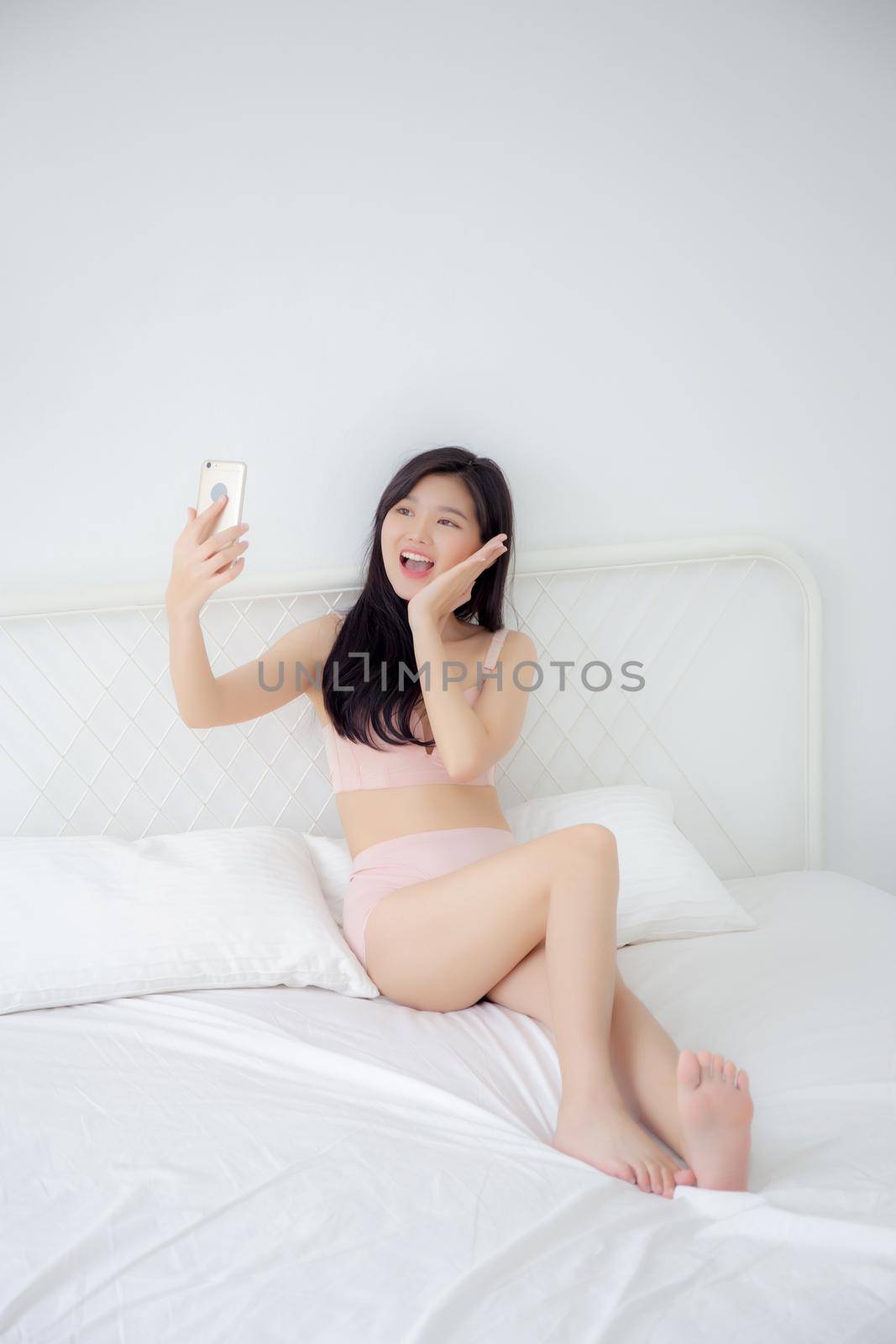 Beautiful young asian woman sexy in underwear talking a selfie on smartphone for social network in the bedroom, girl in lingerie relax with taking a picture on mobile phone on bed in the bedchamber.