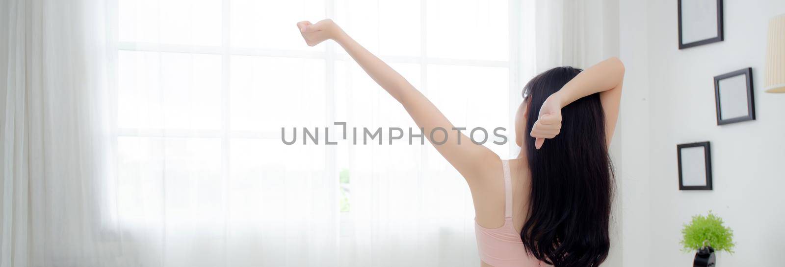 Beautiful young asian woman waking up in the morning and stretching arms  in the bedroom, girl in underwear relax cozy with fresh happy at home, lifestyle concept, back view, banner website. by nnudoo