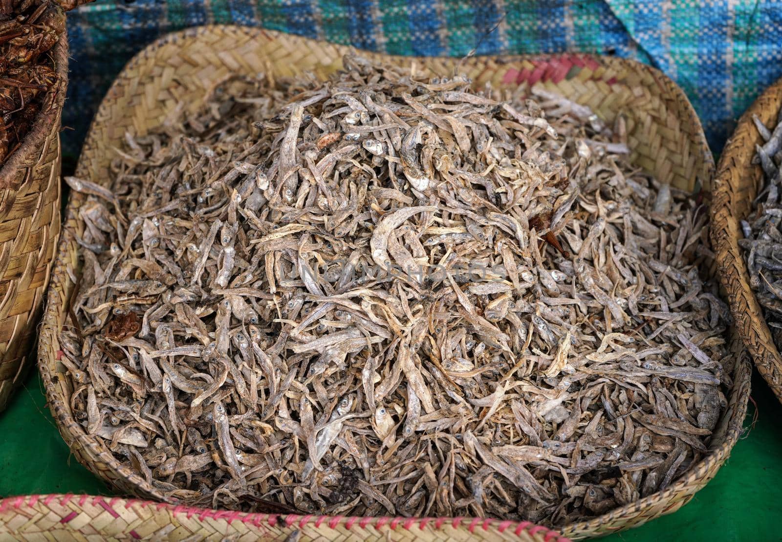 Small dried fish displayed in straw basket on food market at Ranohira, Madagascar, closeup detail by Ivanko