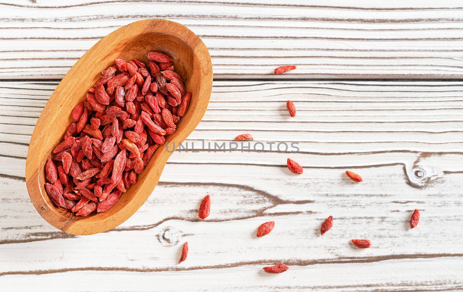 Dried goji aka. wolfberry seeds in wooden bowl and spilled on white boards desk near.
