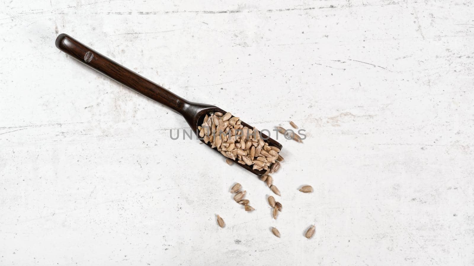 Peeled sunflower seeds in small wooden scoop, placed on white stone like board, view from above by Ivanko