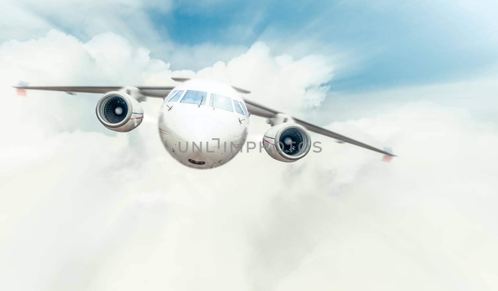 Passenger plane with cockpit and engines in front view flying high in blue cloudy sky. Comfortable and fast travelling by air. Business and touristic trips. Aviation and aircraft.