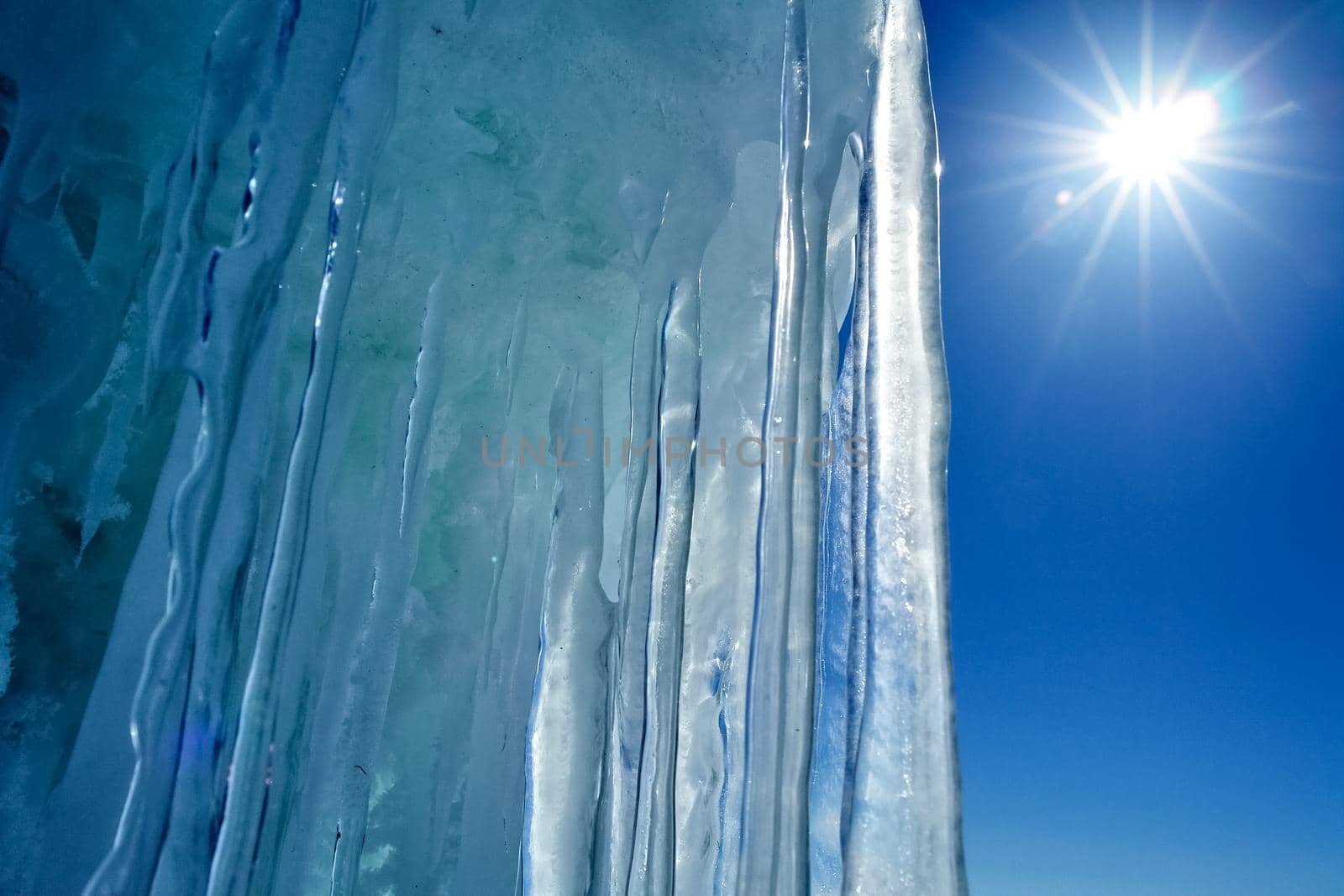 Long icicles made of ice against the blue sky and sun.