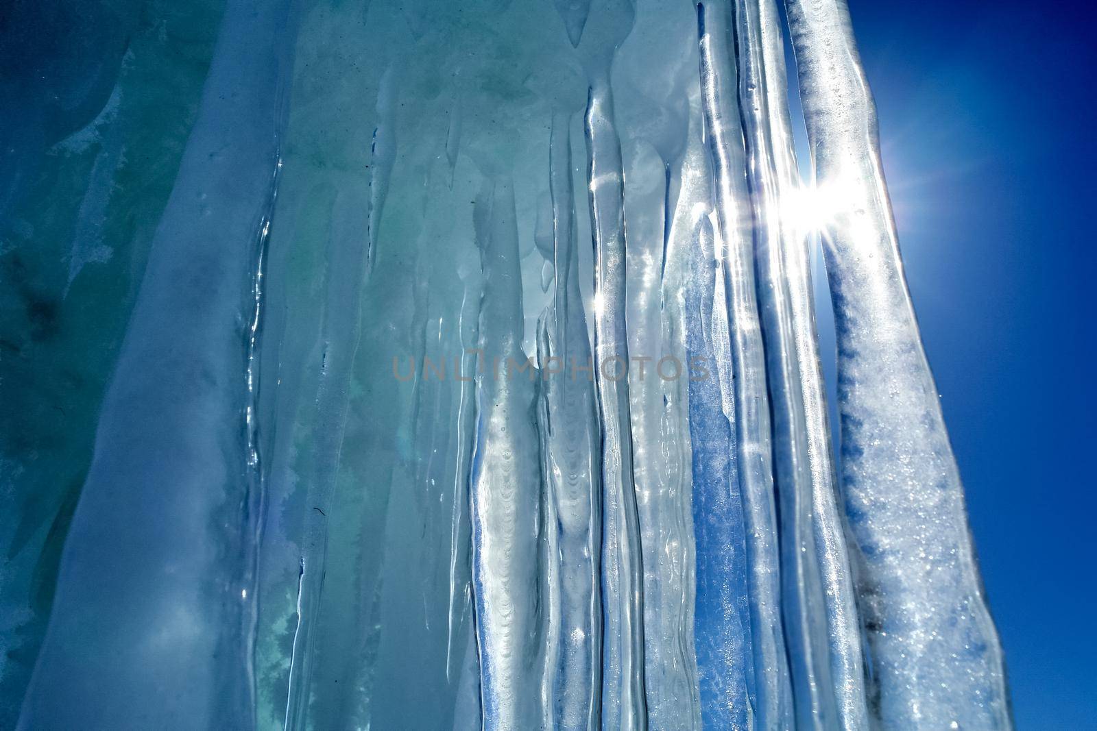 Long icicles made of ice against blue sky and sun. by DePo