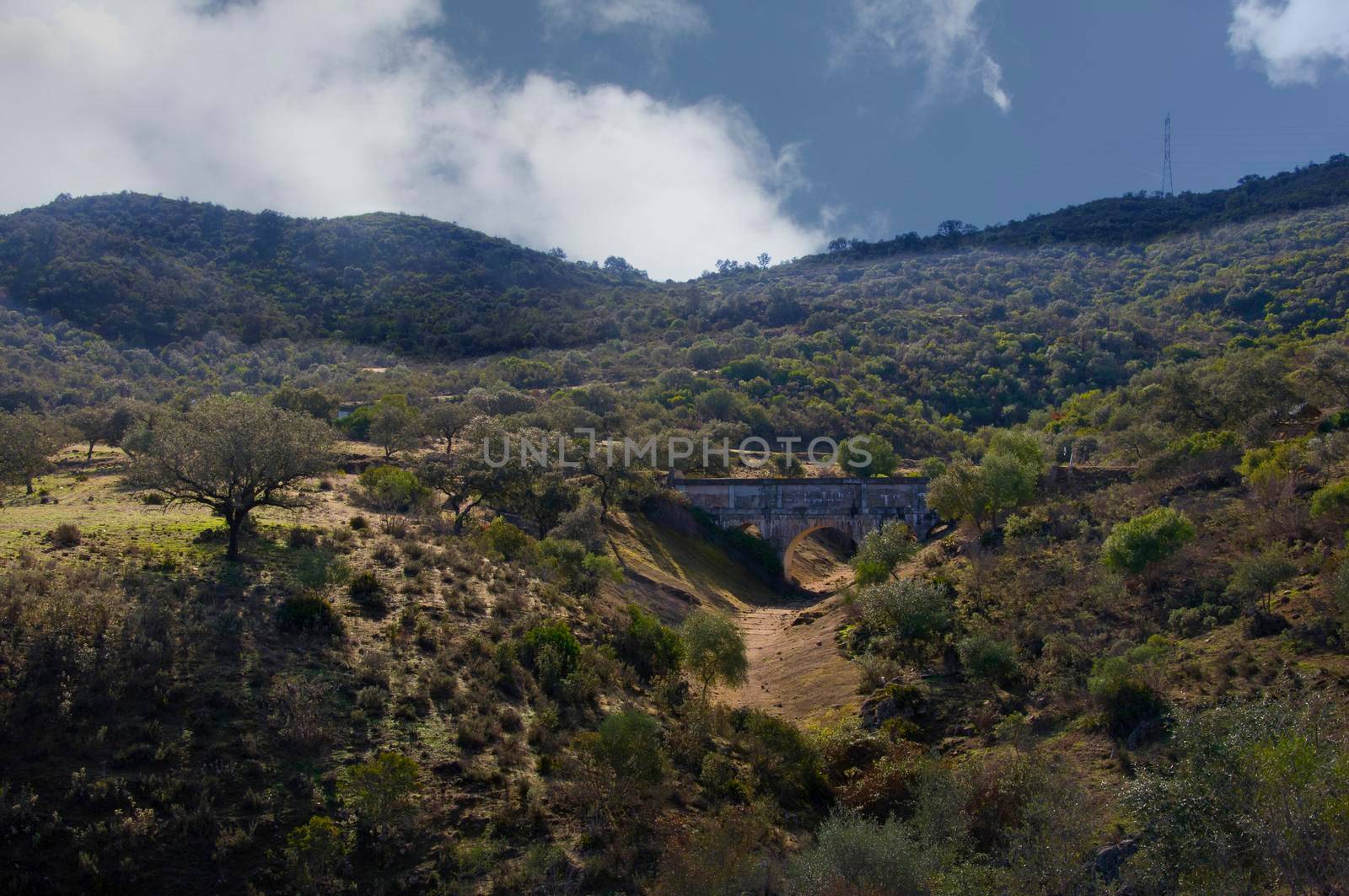 Old stone bridge, green valley and hills. Autumn day, Seville, Spain by Bezdnatm