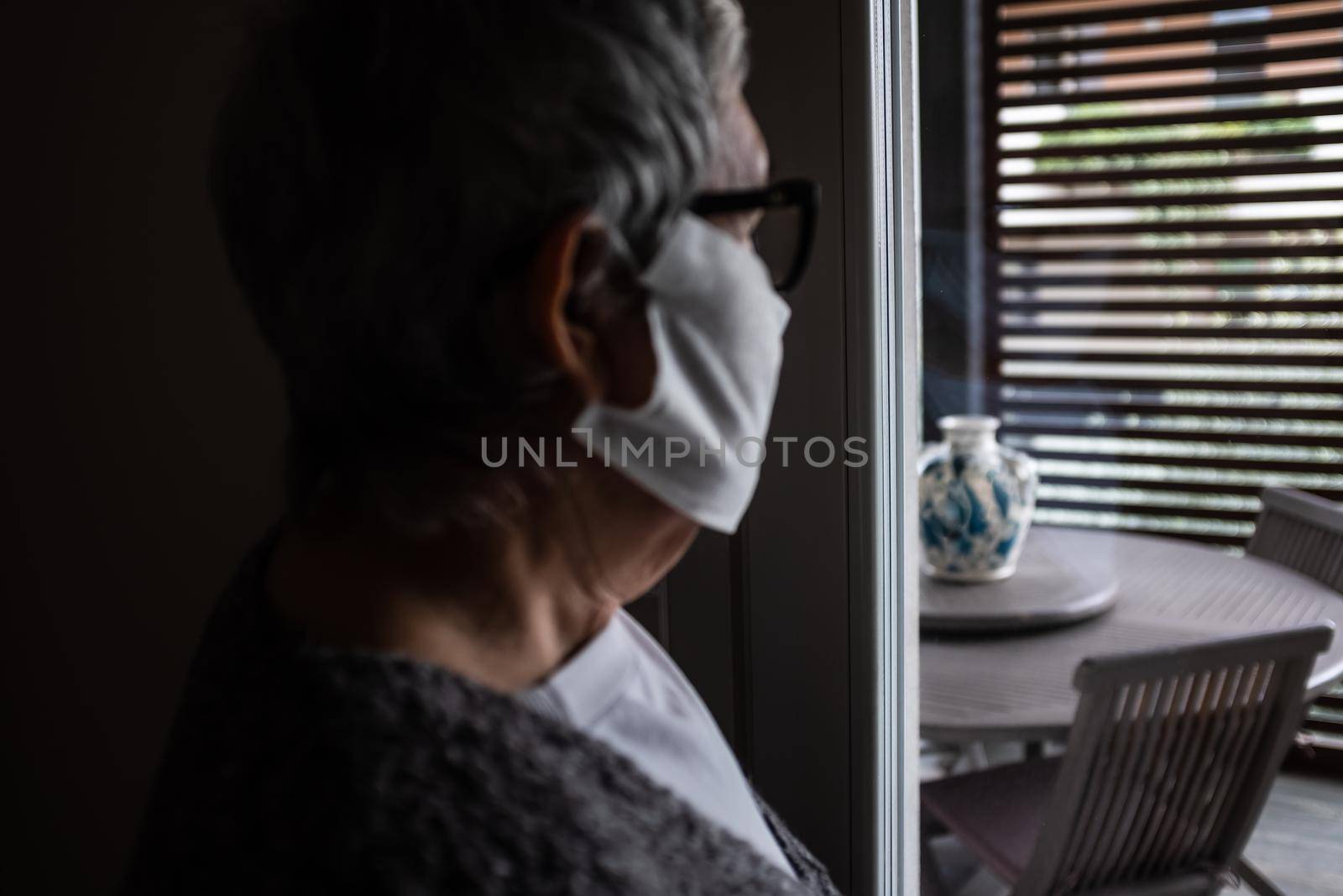 Blurry close-up of a senior adult wearing a protective mask and looking out the window. by Riccarduska