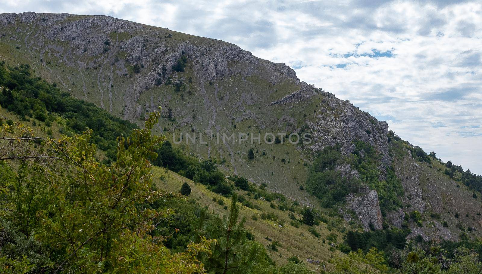 Inaccessible rocks surrounded by green forests and shrubs in hot summers in clear sunny weather.