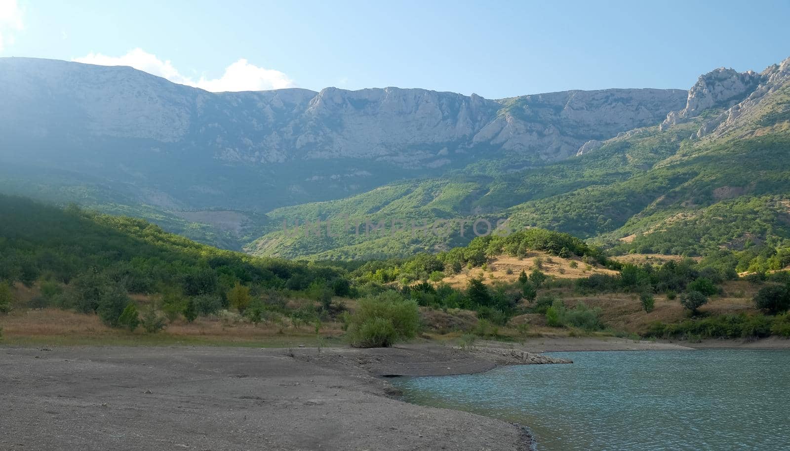 The shore of a mountain lake in the midst of inaccessible rocks, surrounded by a green forest.