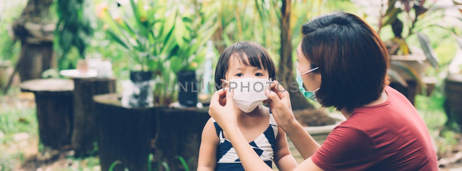 Mother take care daughter with face mask for protection disease flu or covid-19, mom wearing on medical mask with child safety for protect outbreak of pandemic, medical concept, banner website.