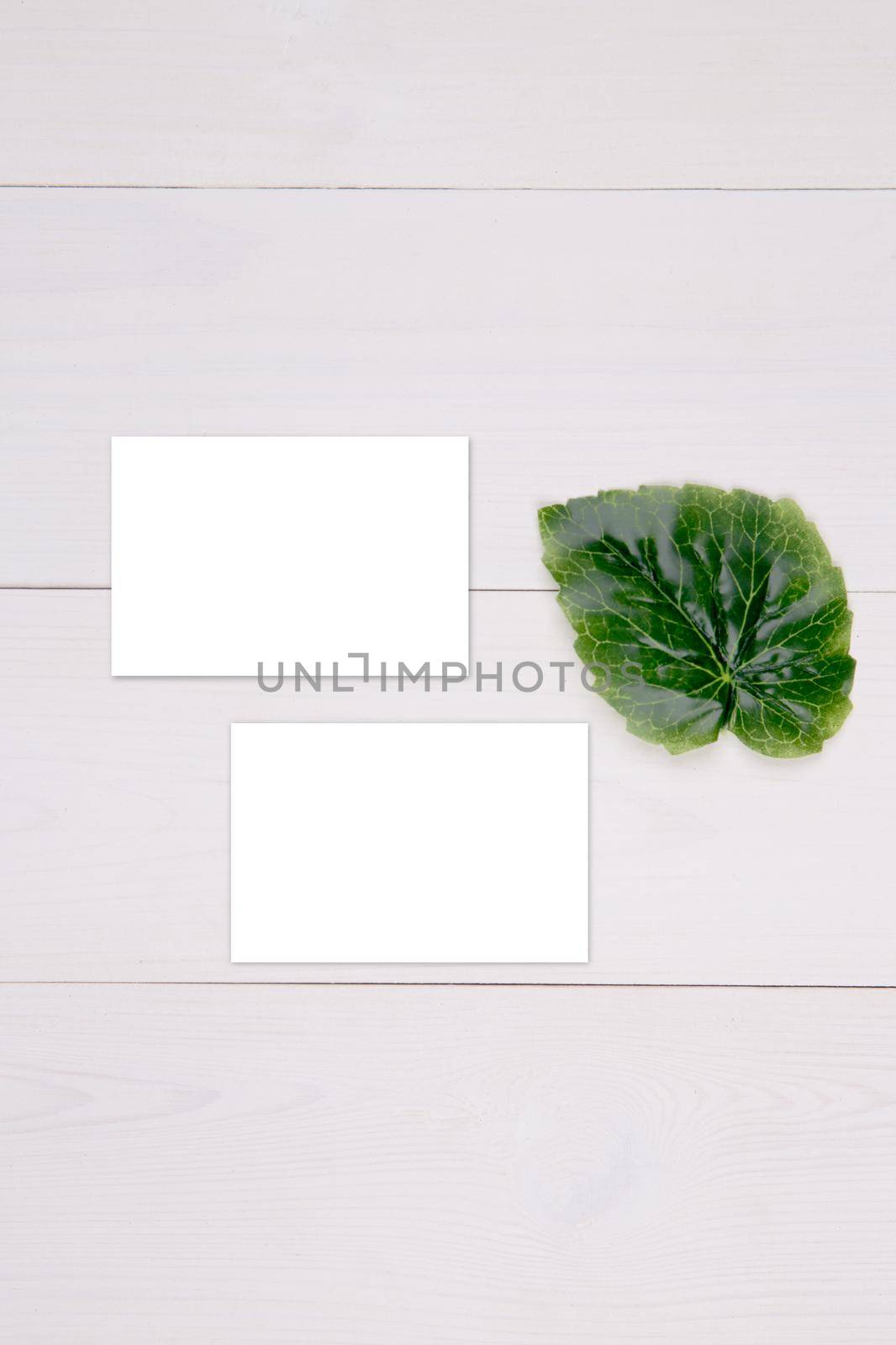 Business card mockup with copy space and leaf on wooden table, name card blank and leaves decoration your design or branding, mock up template, simplicity and minimal, nobody, flat lay, top view. by nnudoo