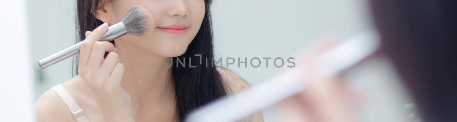 Beauty portrait young asian woman with face looking mirror applying makeup with brush cheek in the bedroom, beautiful girl holding blusher facial, skin care and cosmetic concept, banner website.