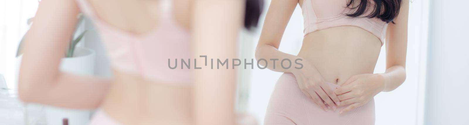 Young asian woman in underwear looking mirror applying cream and lotion on belly, beauty girl diet and weight loss slim applying body care, treatment and cosmetic with moisturizer, banner website.