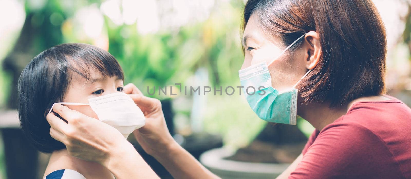 Mother take care daughter with face mask for protection disease flu or covid-19, mom wearing on medical mask with child safety for protect outbreak of pandemic, medical concept, banner website. by nnudoo