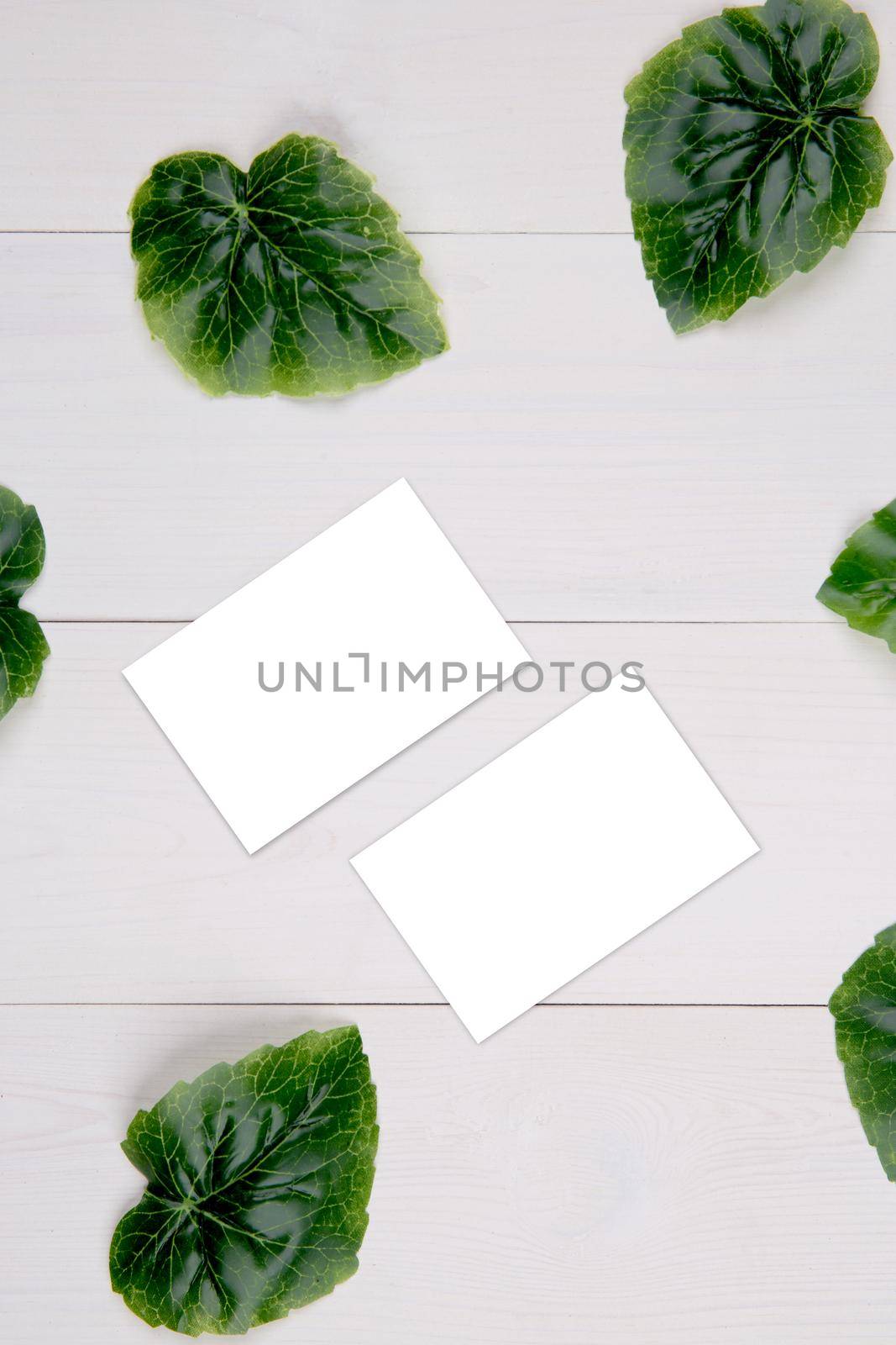 Business card mockup with copy space and leaf on wooden table, name card blank and leaves decoration your design or branding, mock up template, simplicity and minimal, nobody, flat lay, top view. by nnudoo