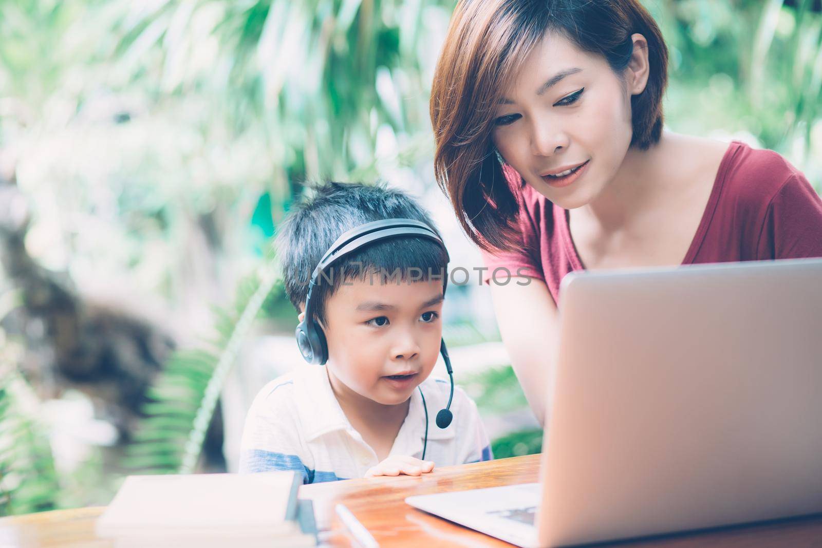 Young asian mother and son using laptop computer for study and learning together at home, boy wearing headphone for e-learning with distancing, teacher or mom support child, education concept. by nnudoo
