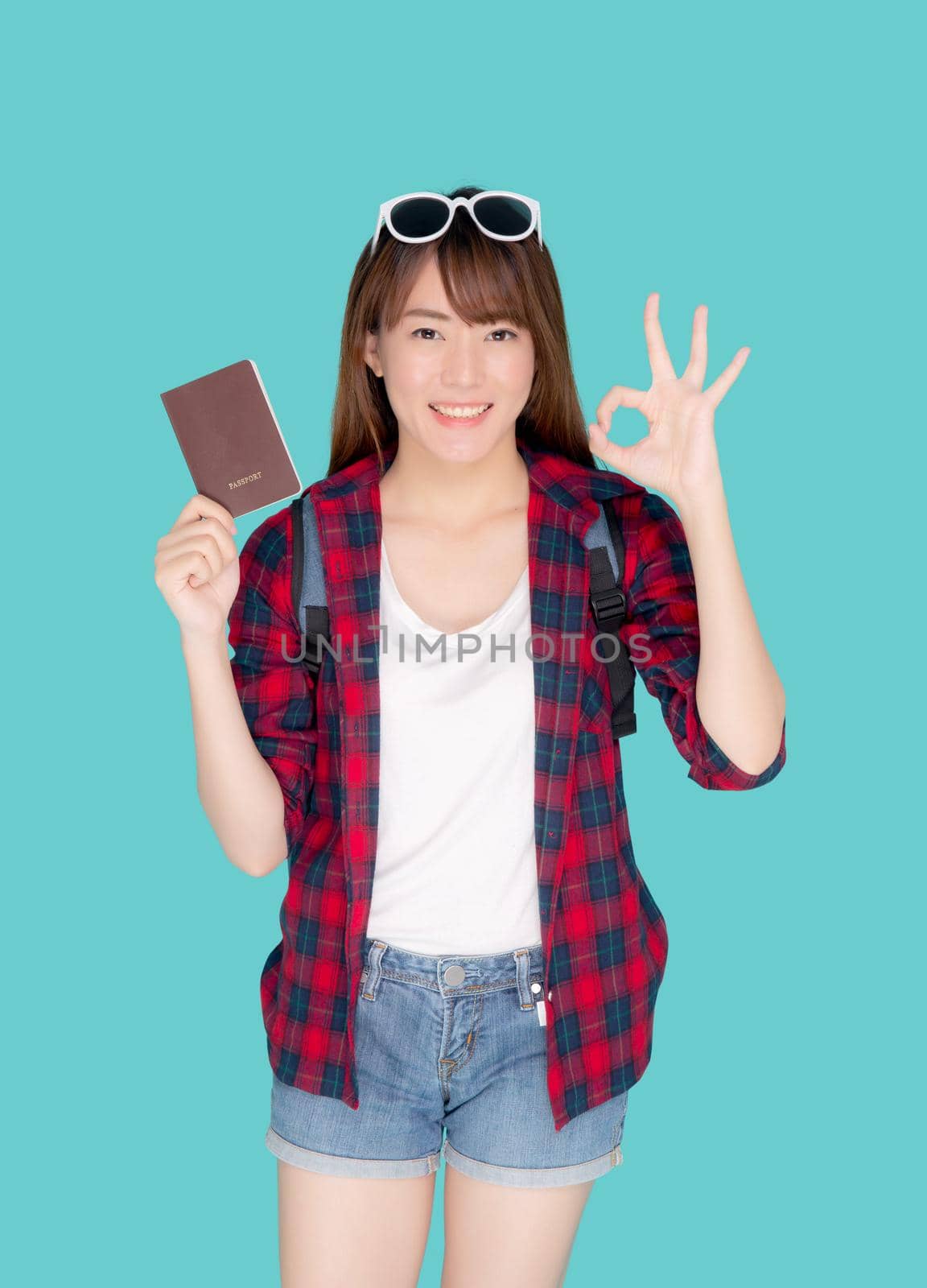 Beautiful portrait young asian woman wear sunglasses on head and backpack smiling gesture ok enjoy summer travel holiday isolated blue background, asia girl fashion trip and holding passport.