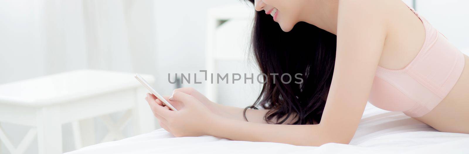 Young asian woman sexy in underwear chatting on mobile phone in the bedroom, girl in lingerie looking social media on smartphone lying on bed, communication and lifestyle concept, banner website.