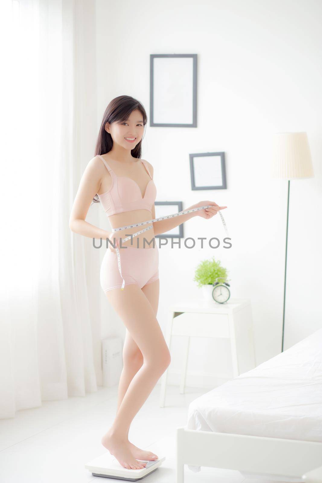 Beautiful young asian woman sexy body slim standing on scales measuring abdomen for control weight loss in the room, beauty girl belly thin have cellulite with tape measure for diet, health concept.