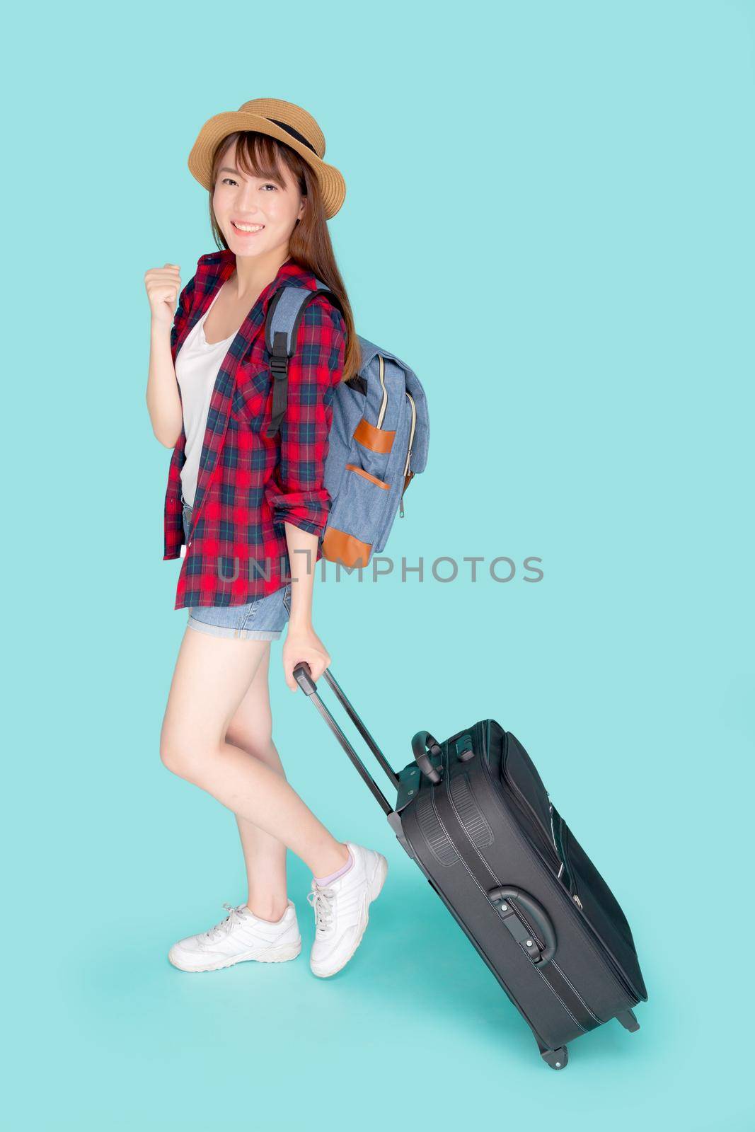 Beautiful young asian woman pulling suitcase isolated on blue background, asia girl having expression cheerful and success holding luggage walking in vacation with excited, journey and travel concept.