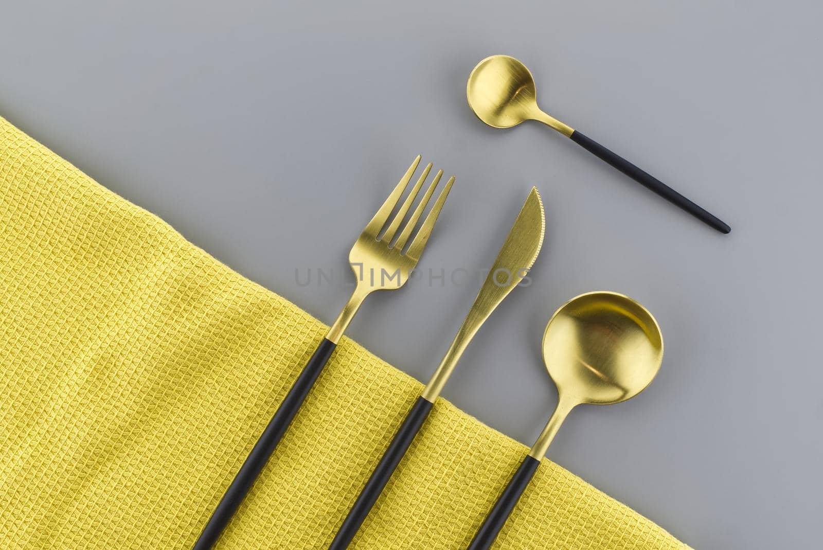 Set of stylish black and gold cutlery on a two tone grey and yellow background with copy space viewed as a flat lay. Main color trend of the year