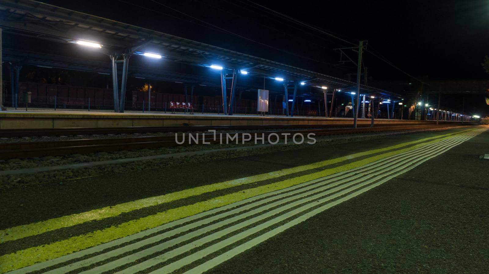 Line of hazard warning tactile paving along the edge of platform at the train station at night