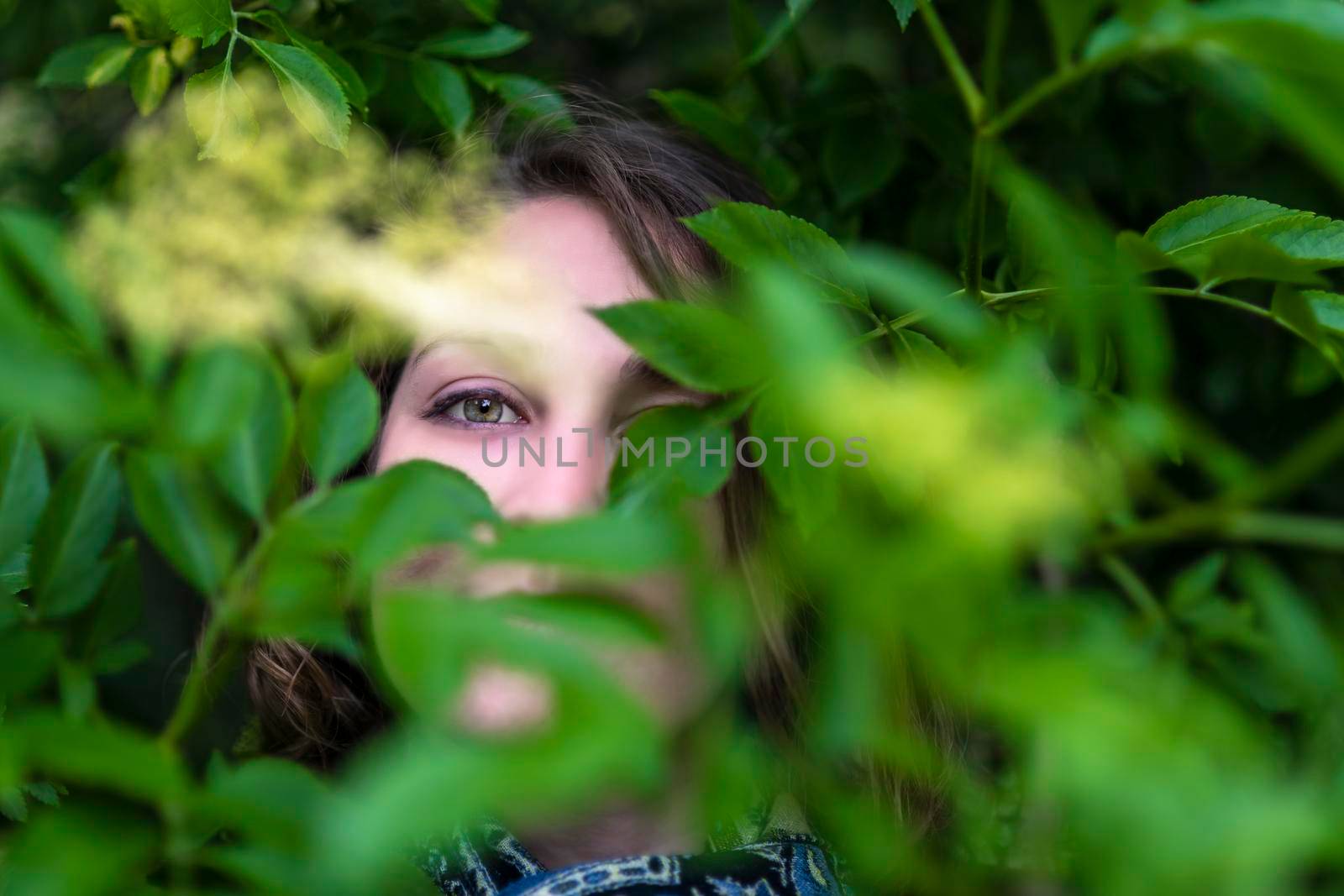 Young woman poses among the plants, watching and camouflaging.