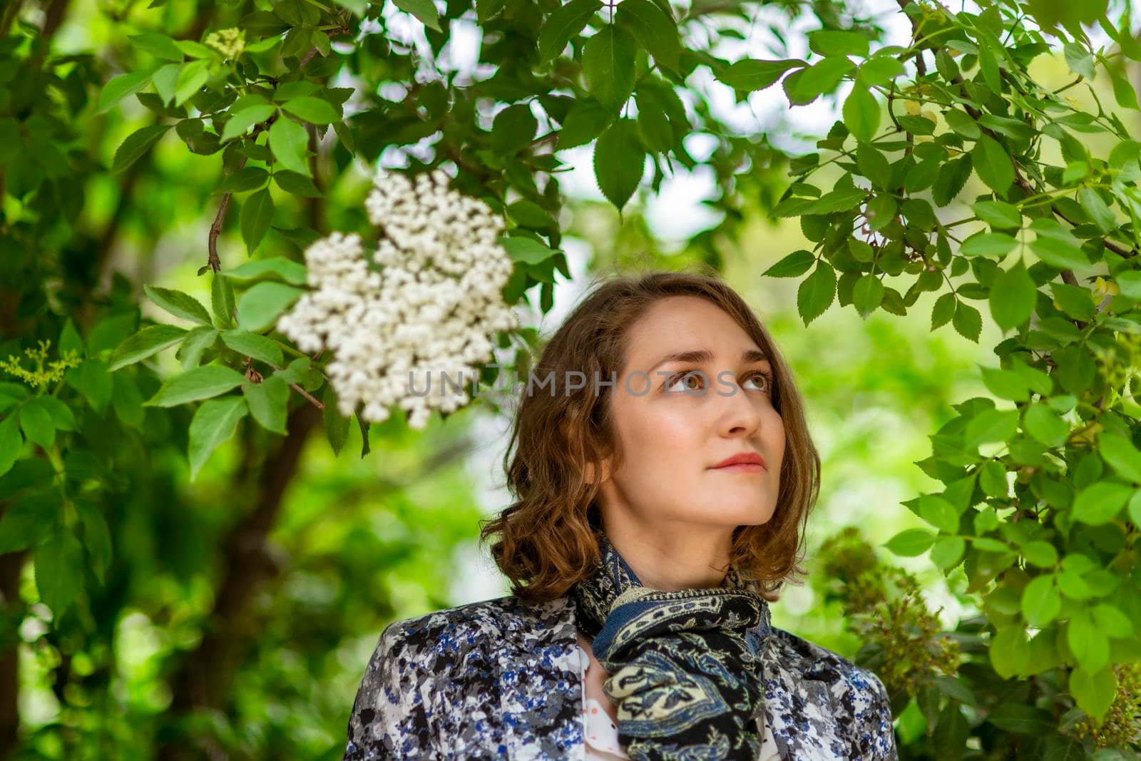 Young woman poses among the plants, looking at one of them.