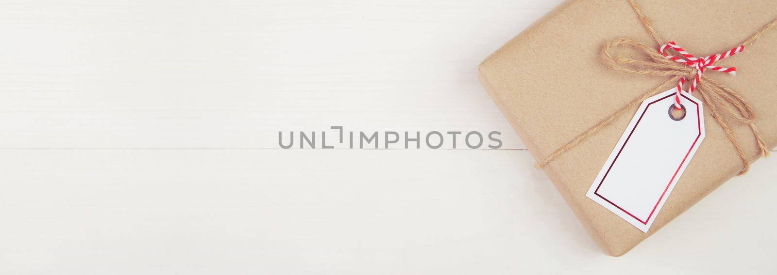 Gift box with kraft paper and tag or label on wooden table in Christmas day or holiday, present box for anniversary celebration with copy space, celebrate and festive, flat lay, banner website. by nnudoo