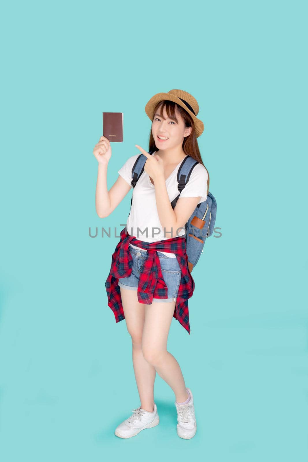 Beautiful portrait young asian woman wear hat smile confident holding and pointing passport with travel summer trip in vacation isolated blue background, model tourist hipster asia girl cheerful.