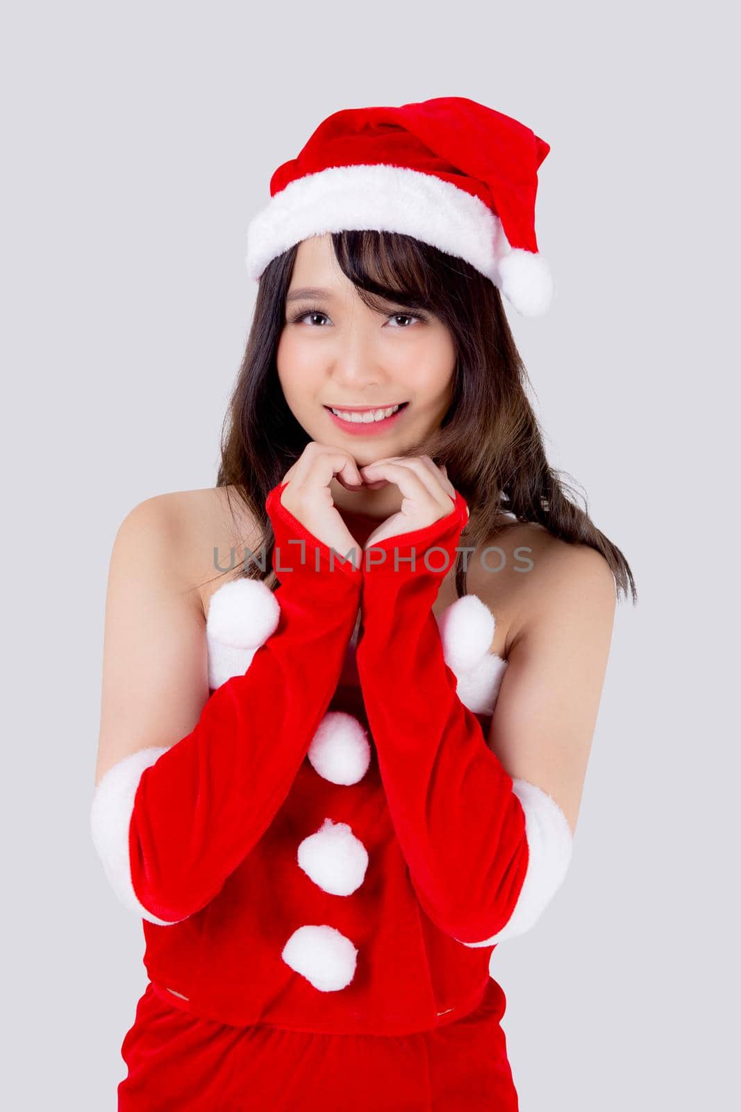 Beautiful portrait young asian woman Santa costume wear hat smiling gesture heart with hand in holiday xmas, beauty model asia girl cheerful celebrating in Christmas isolated on white background.