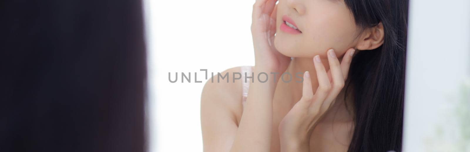 Beautiful young asian woman look at mirror of checking face with skin care and cosmetic for hygiene, beauty girl happy clean facial with cream or lotion and for health, banner website.