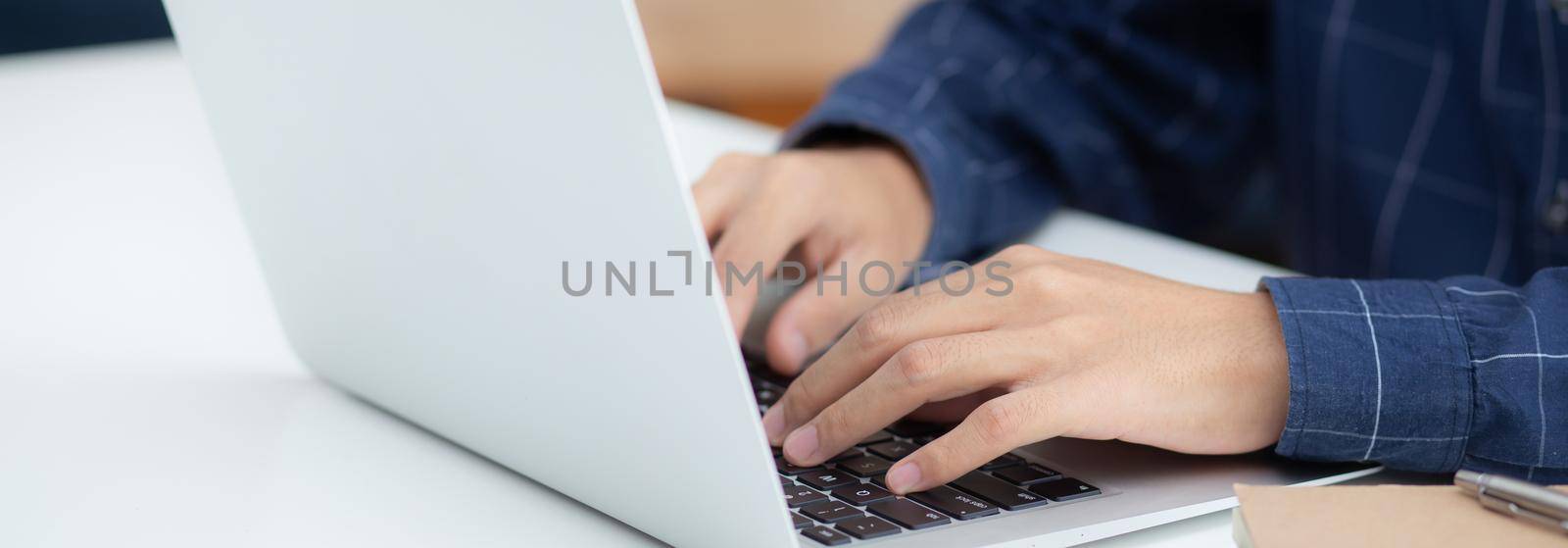 Employee young man typing and working on laptop computer on desk at home, business man using notebook and check email on table, hand of freelance is blogger, lifestyle concept, banner website. by nnudoo