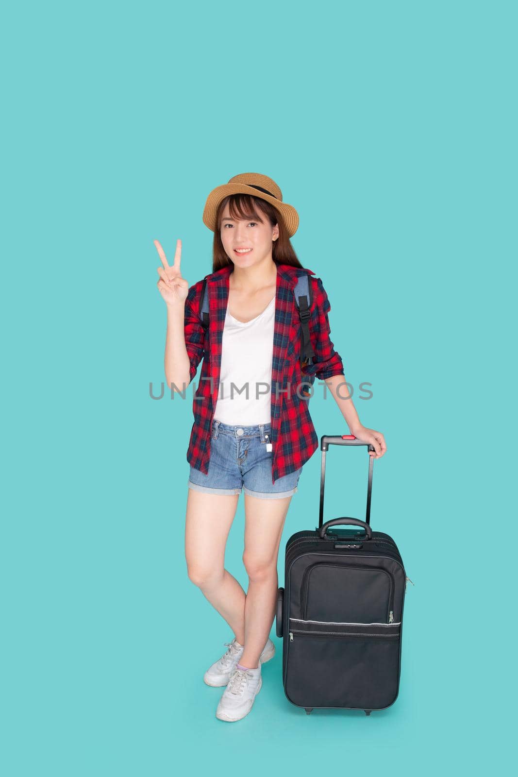 Beautiful young asian woman pulling suitcase isolated on blue background, asia girl cheerful holding luggage walking and gesture ok in vacation with excited, journey and travel concept. by nnudoo