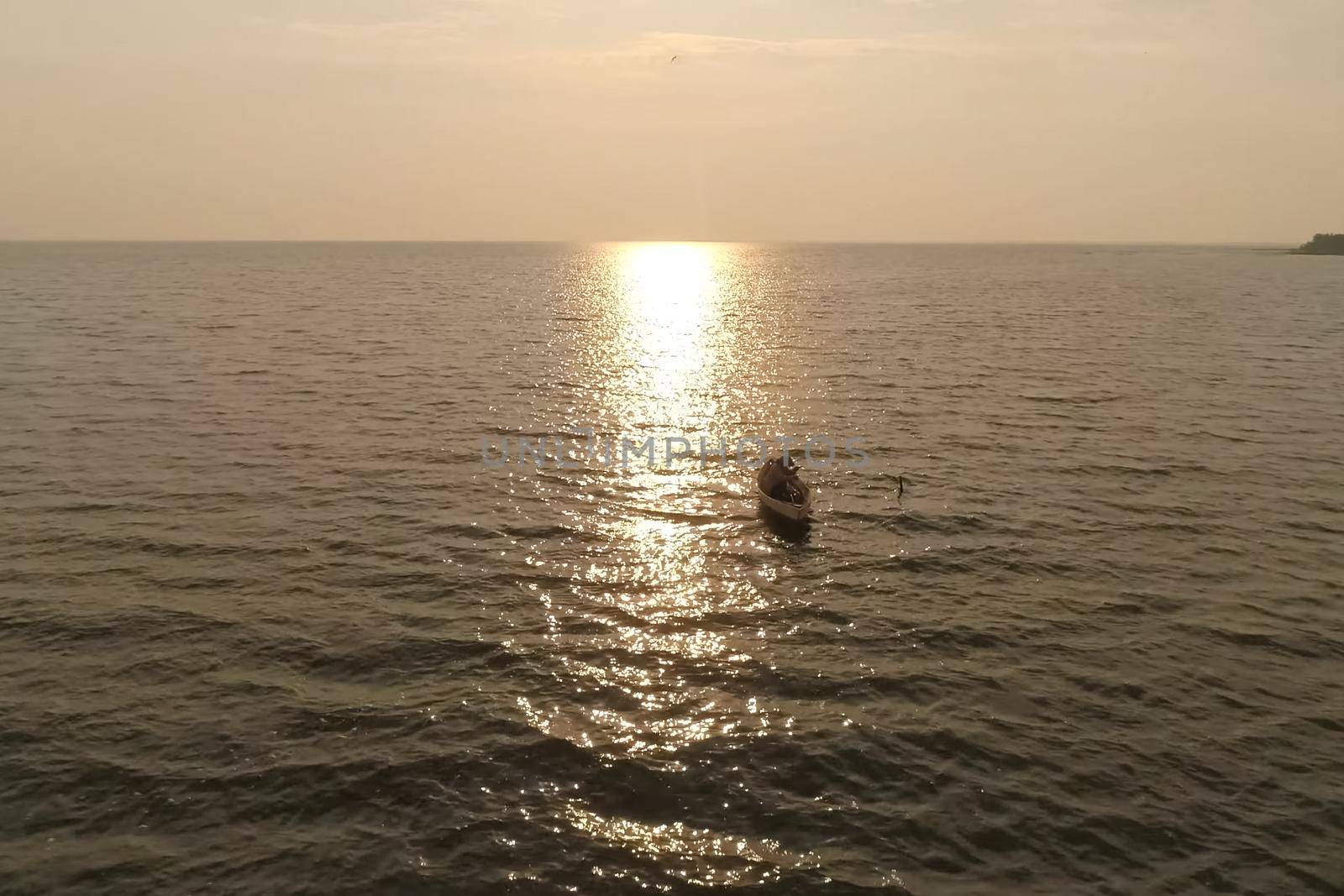 A fisherman in a boat in the sea against the sunset.