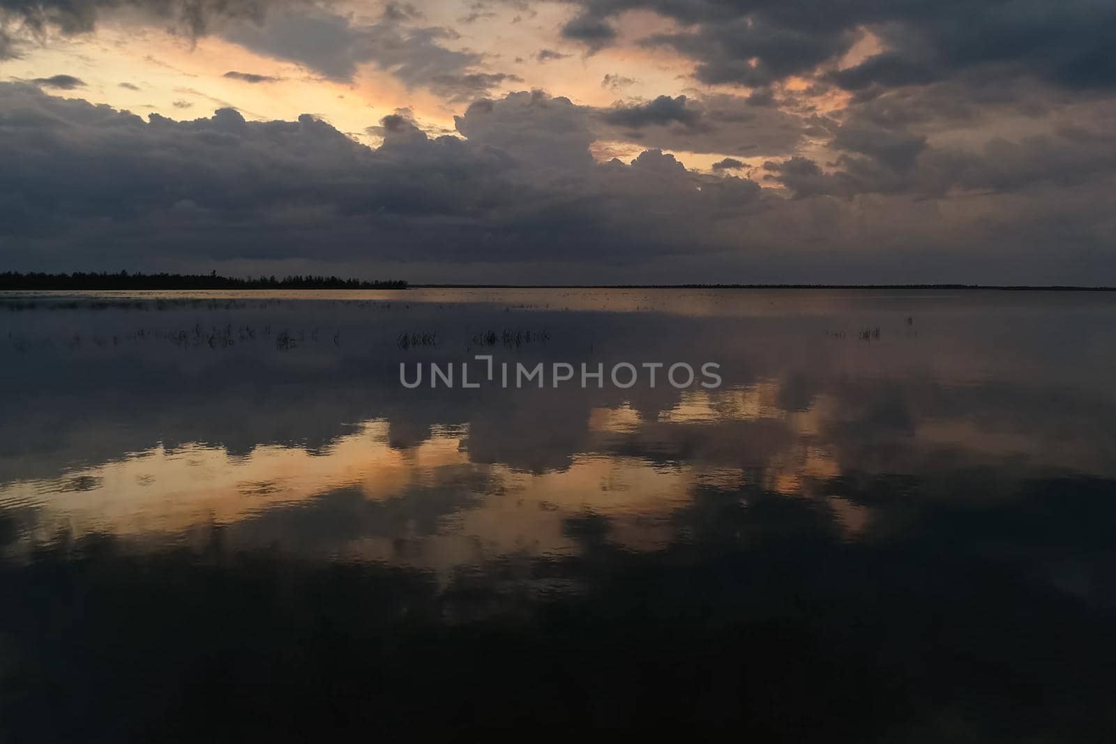 The sky is in zagon with clouds above the pond. Sunset time.