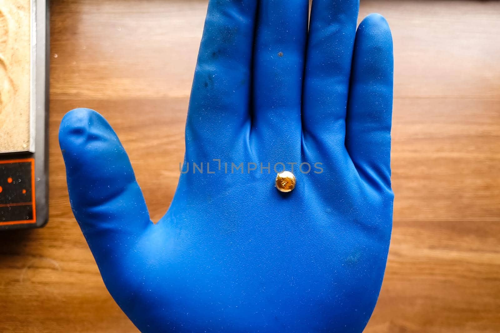 A small piece of gold in his hand with a glove. Mini nugget of gold.