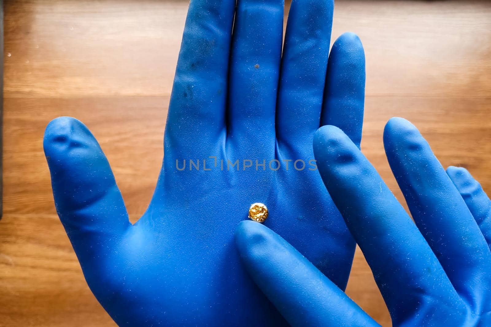 A small piece of gold in his hand with a glove. Mini nugget of gold.