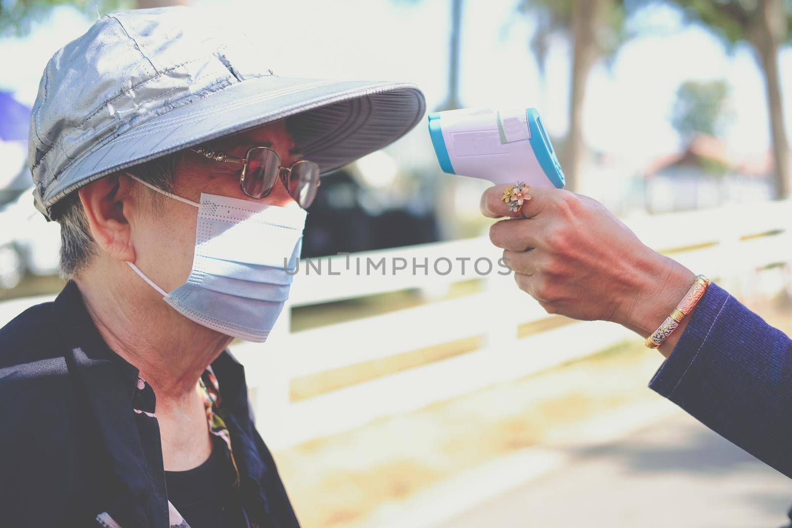 hand measuring body temperature of old woman with infrared forehead thermometer gun