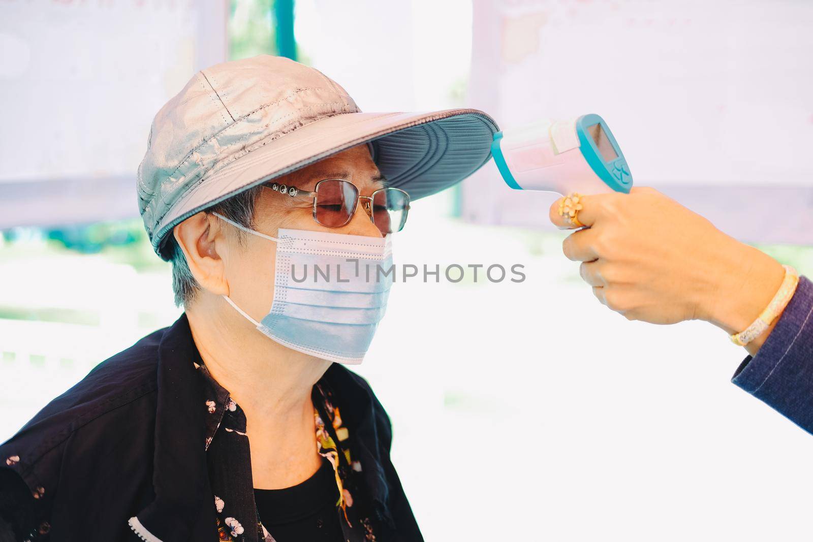 hand measuring body temperature of old woman with infrared forehead thermometer gun