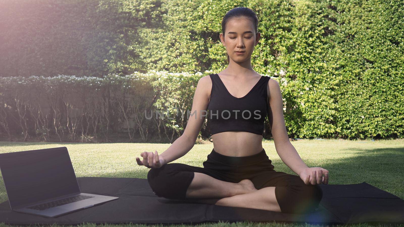 A sporty woman or online instructor in sportswear is sitting and practicing yoga  by gnepphoto