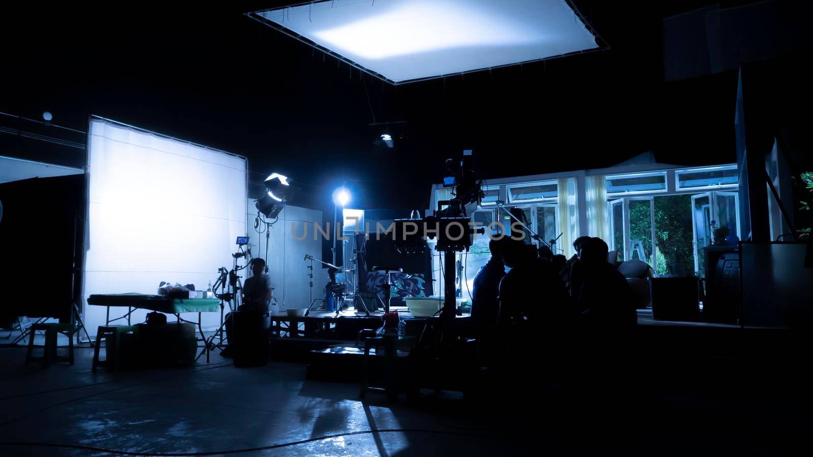 Silhouette images of video production behind the scenes or b-roll or making of TV commercial movies that film crew team lightman and videos cameraman working together with movie director in studio.