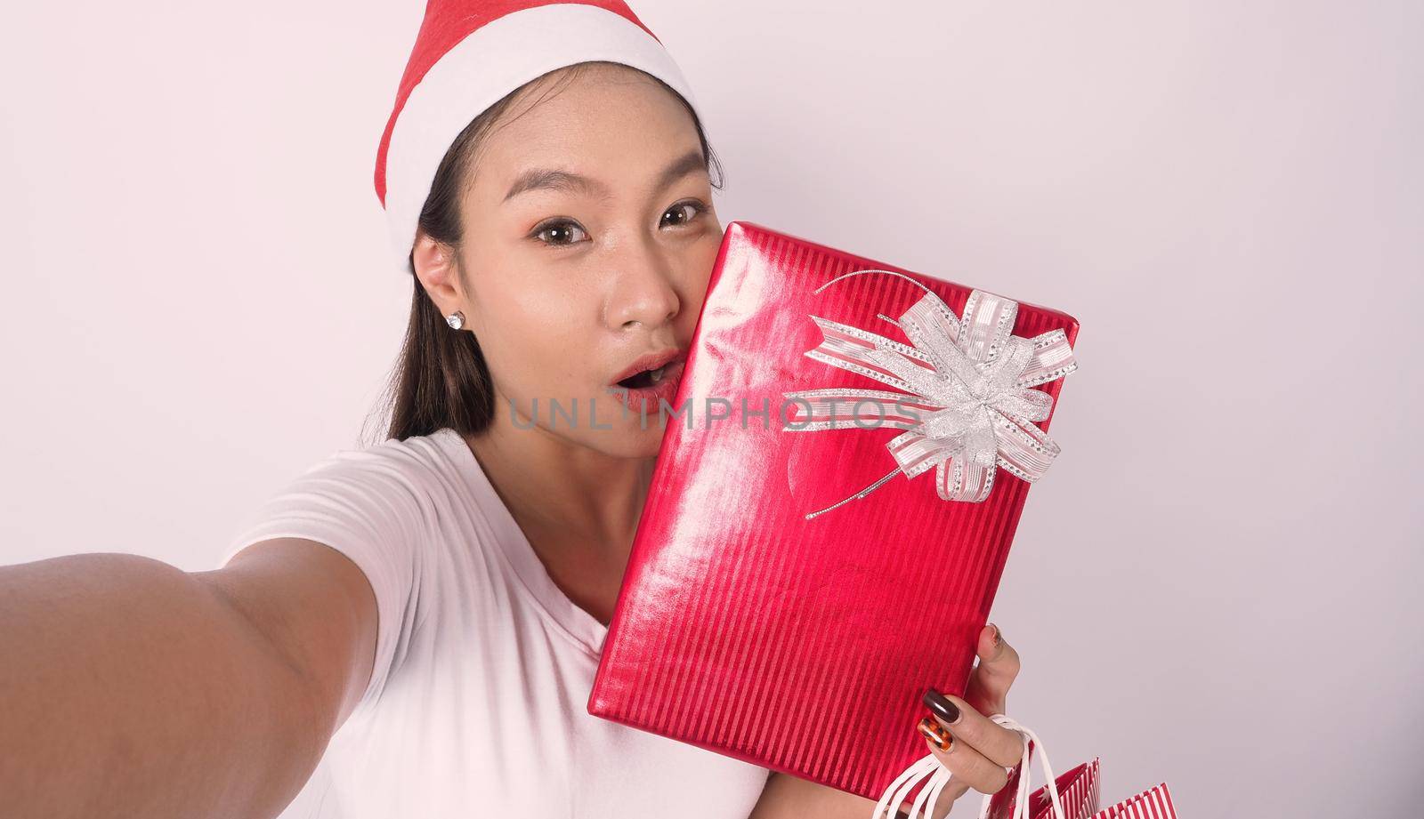 Girl hold gift box make selfie or video online with x-mas christmas prop decoration. Asian Thai teen woman taking online-selfie to celebrate festive season with her friend by red giftbox. studio shot.
